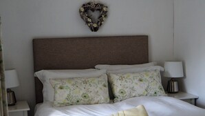 A neatly made bed with floral pillows, a heart-shaped wall decoration, and bedside lamps. - Historic remodelled stable barn near nature conservation (Pulborough)