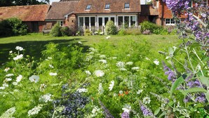 A traditional brick house with a large garden in front, featuring various flowers and a wooden fence. - Historic remodelled stable barn near nature conservation (Pulborough)