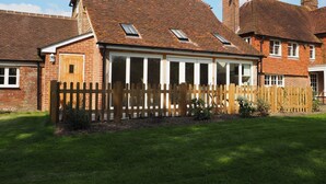 A two-story brick house with a sloped roof, a wooden fence, and a grassy yard. - Historic remodelled stable barn near nature conservation (Pulborough)