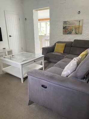 A living room with a grey sofa, a white coffee table, and a painting on the wall. - Historic remodelled stable barn near nature conservation (Pulborough)