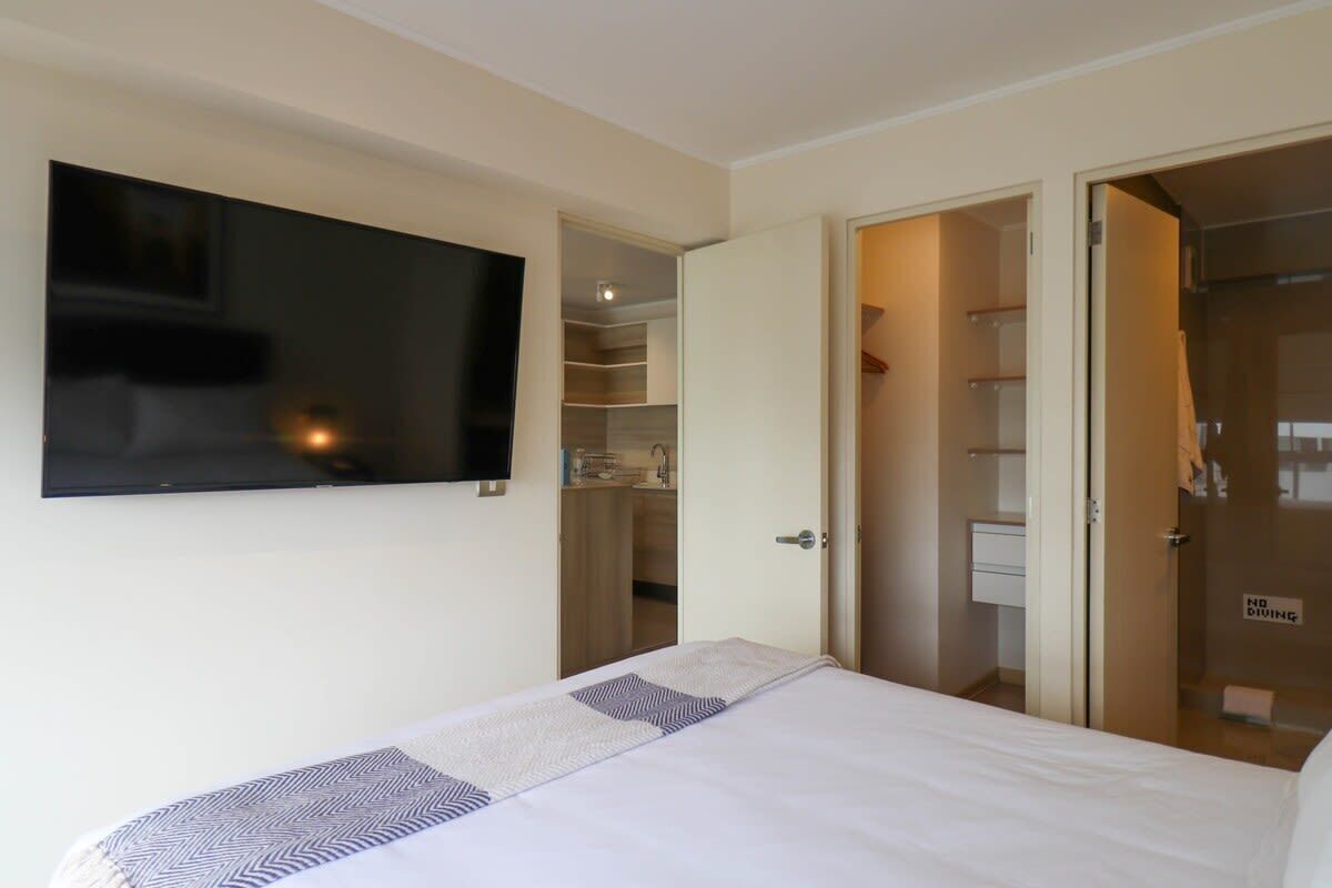 A hotel room with a bed, a television mounted on the wall, and an open closet with a 'No Diving' sign.