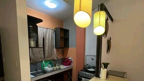 Une cuisine compacte dotée d’un îlot central, d’une cuisinière et de luminaires suspendus.