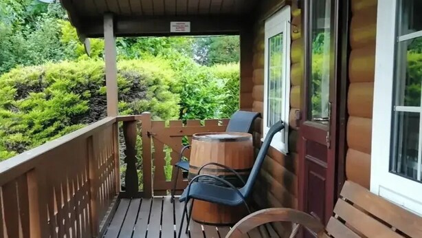 Une terrasse en bois avec un banc en bois et un tonneau, le tout entouré d’une végétation luxuriante.