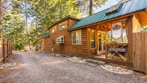 A rustic cabin with a metal roof, a welcome sign, and a gravel driveway. - Das Tree Haus 1 Bedroom Home by NW Comfy Cabins by RedAwning (Leavenworth)