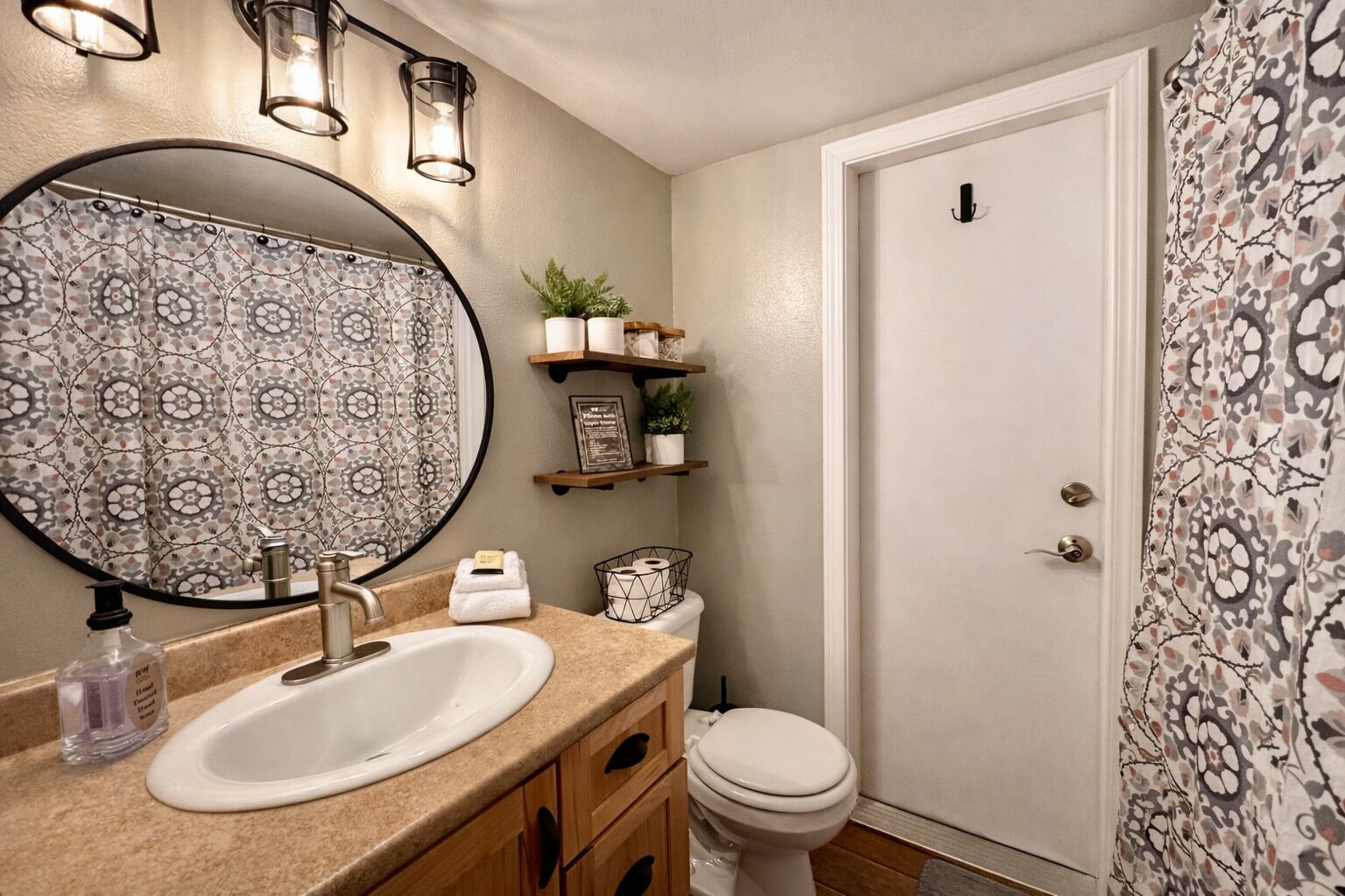 A bathroom with a round mirror, a sink, a toilet, and a door.
