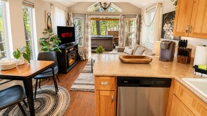 A modern kitchen with a dishwasher, coffee maker, and a dining area with a TV displaying 'NETFLIX'. - Das Tree Haus 1 Bedroom Home by NW Comfy Cabins by RedAwning (Leavenworth)
