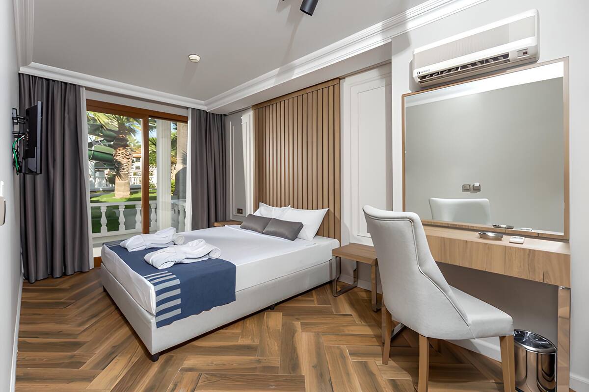 Habitación de hotel con cama, escritorio, silla, espejo y aire acondicionado.