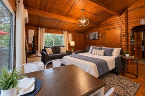 A cozy log cabin bedroom with a bed, a sofa, a dining table, and a window.