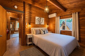 Un dormitorio de cabaña de madera con cama, mesita de noche y ventana con cortinas.