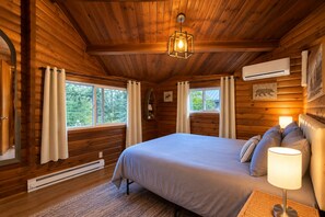 A log cabin bedroom with a bed, curtains, a window, a wall-mounted air conditioner, and a bear picture. - A Peace Of Pine 2 Bedroom Home by NW Comfy Cabins by RedAwning (Leavenworth)