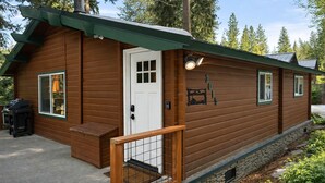 Una baita di legno con una porta d'ingresso, due finestre, un portico e un barbecue all'esterno.