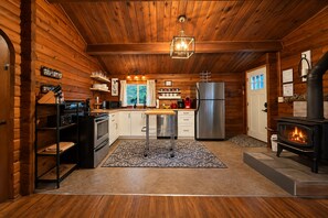 A log cabin interior with a kitchen, dining area, and a wood-burning stove. - A Peace Of Pine 2 Bedroom Home by NW Comfy Cabins by RedAwning (Leavenworth)