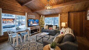 En mysig stuga med träpanel i taket, en tv på ett träbord, en soffa, ett soffbord och en julgran.
