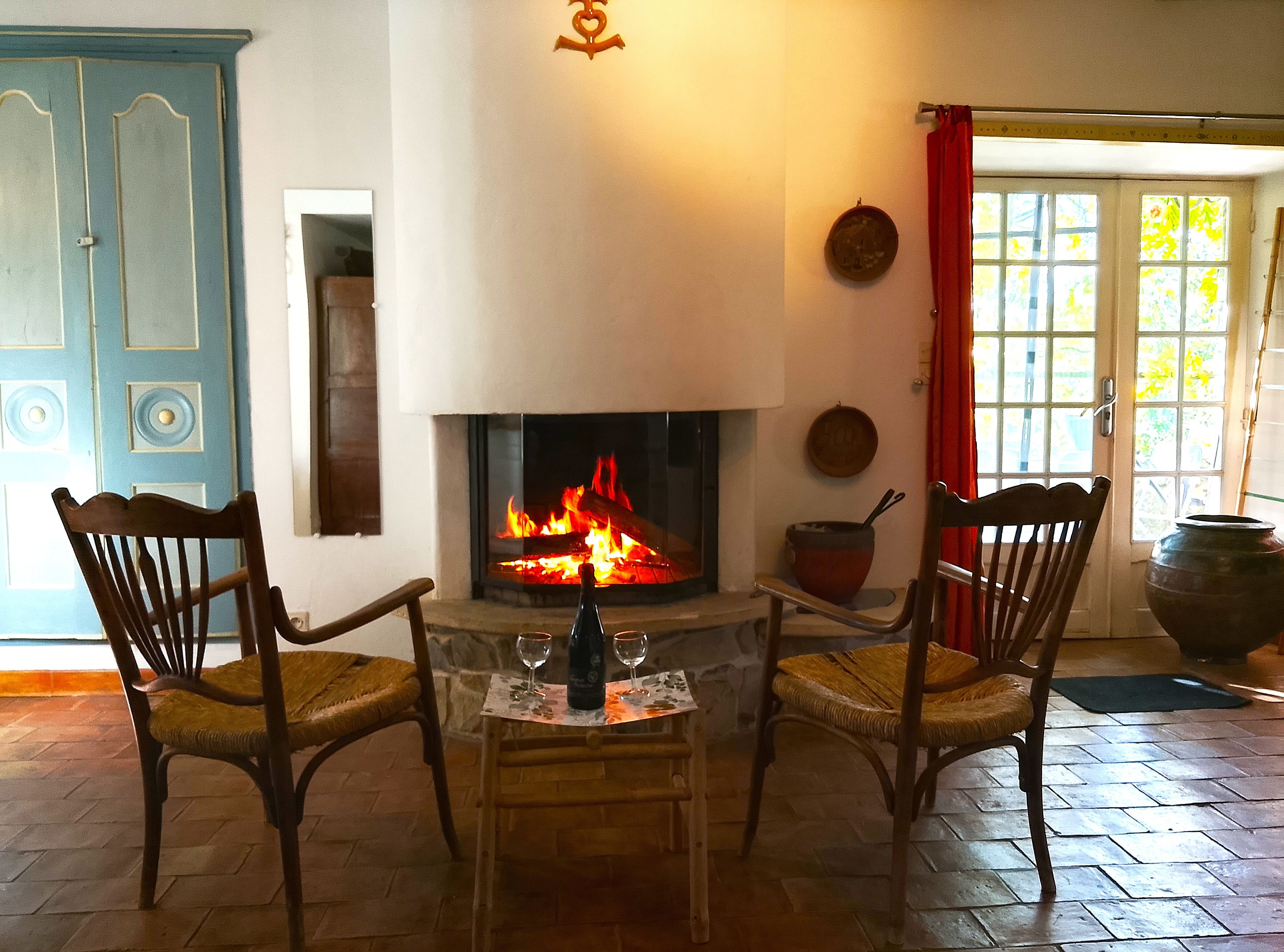 Une pièce avec une cheminée, deux chaises en bois, une table avec une bouteille et des verres, et une porte ornée d’une plaque décorative.