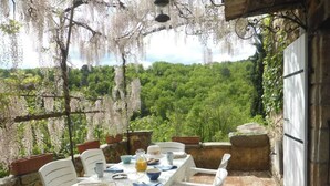 An outdoor dining area with a table set for two, surrounded by white chairs, overlooking a lush green forest. - Charming detached house with terrace in a farmhouse with swimming pool and garden (Vesseaux)
