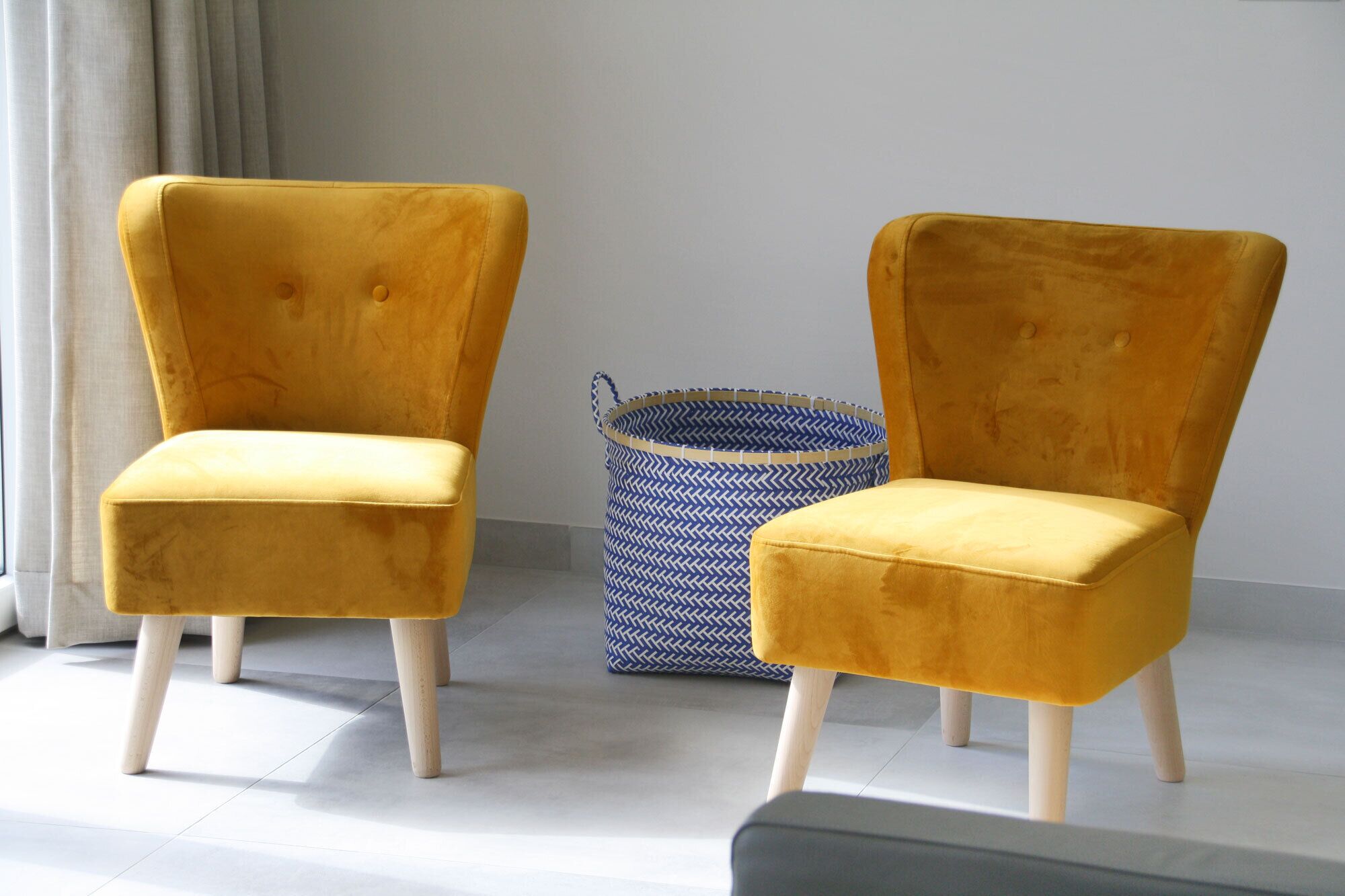 Two mustard-colored armchairs with wooden legs and a woven basket in the background.