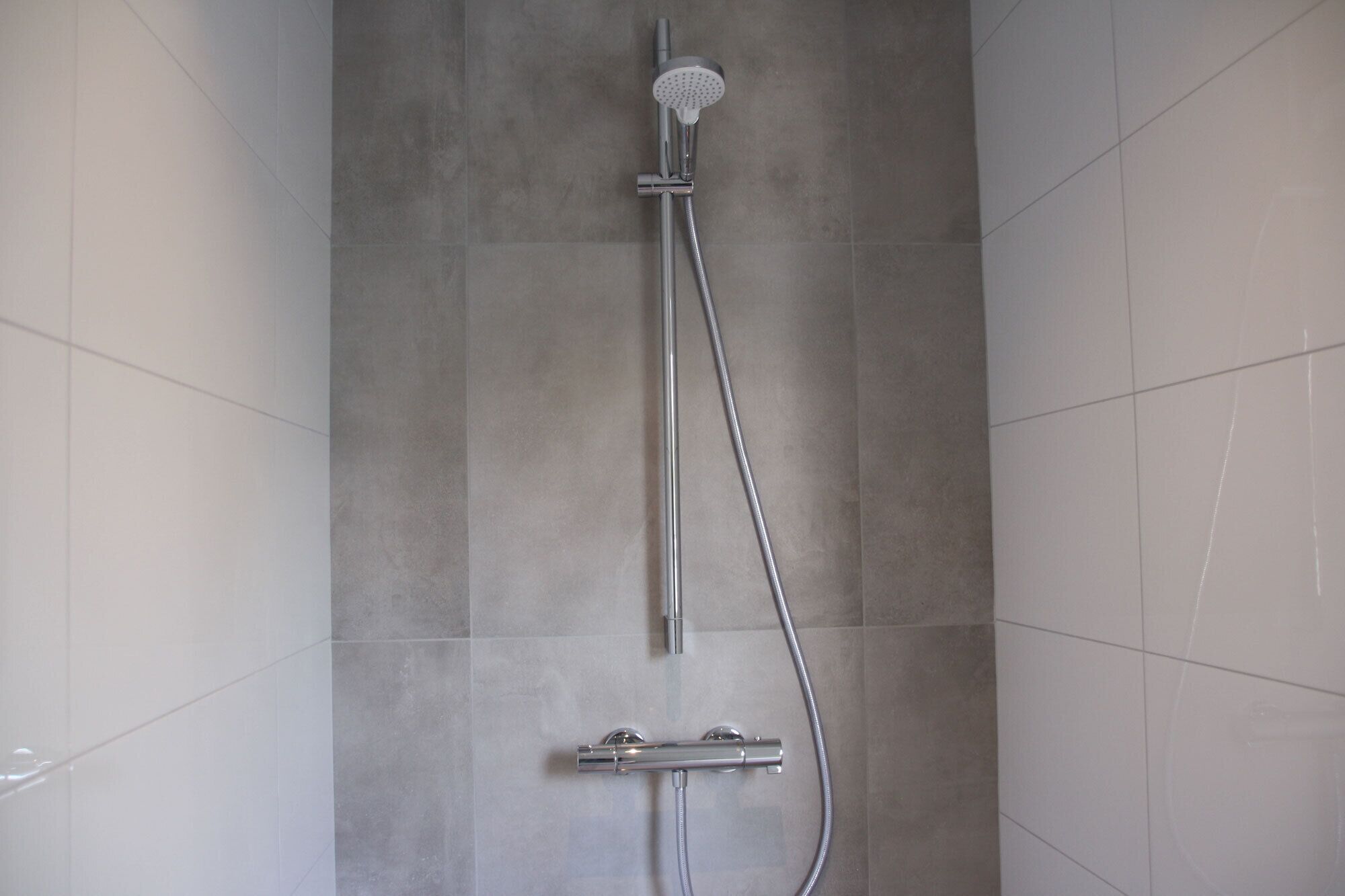 Een douche met een handdouche en een bedieningspaneel aan de muur.