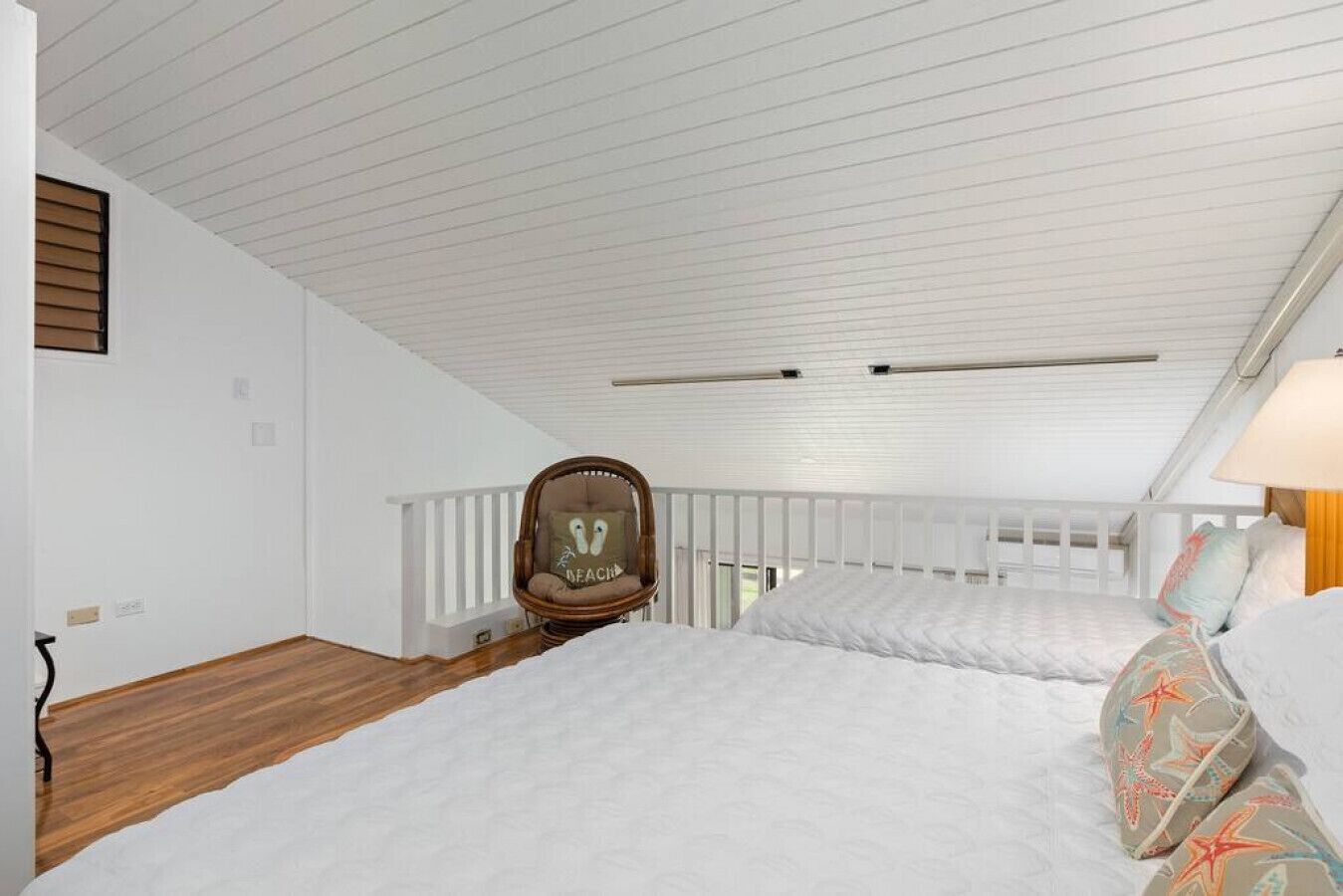 A bedroom with a sloped ceiling, a wooden floor, a white bed, a rocking chair, and a view of the outdoors.
