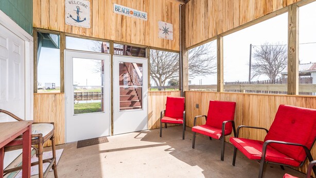 L’intérieur est en bois et on y trouve une pancarte « Bienvenue », une autre indiquant « Maison de plage » et une boussole. Il y a des chaises rouges et une table en bois.