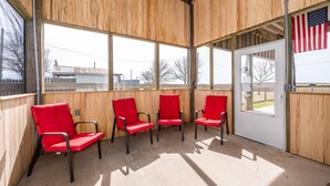 Une salle d’attente aux murs en bois, dotée de grandes fenêtres et de trois chaises rouges.