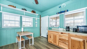Une cuisine aux murs de couleur turquoise, avec des meubles en bois, une table en bois accompagnée de bancs et une fenêtre munie de stores.