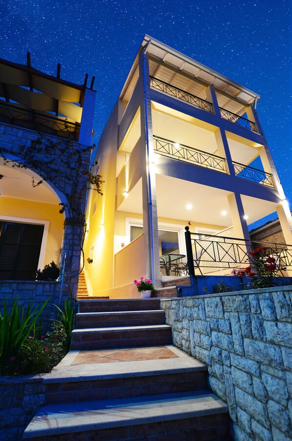 A multi-story building with a balcony, steps leading to the entrance, and a starry night sky. - Meltemi Studios (Lefkada)