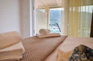 Habitació d'hotel amb un llit, una tovallola doblegada, una manta amb textura i vista al mar a través d'un balcó amb barana.