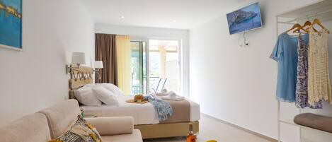 A modern hotel room with a bed, a sofa, a table with fruit and a bottle, and a clothing rack.