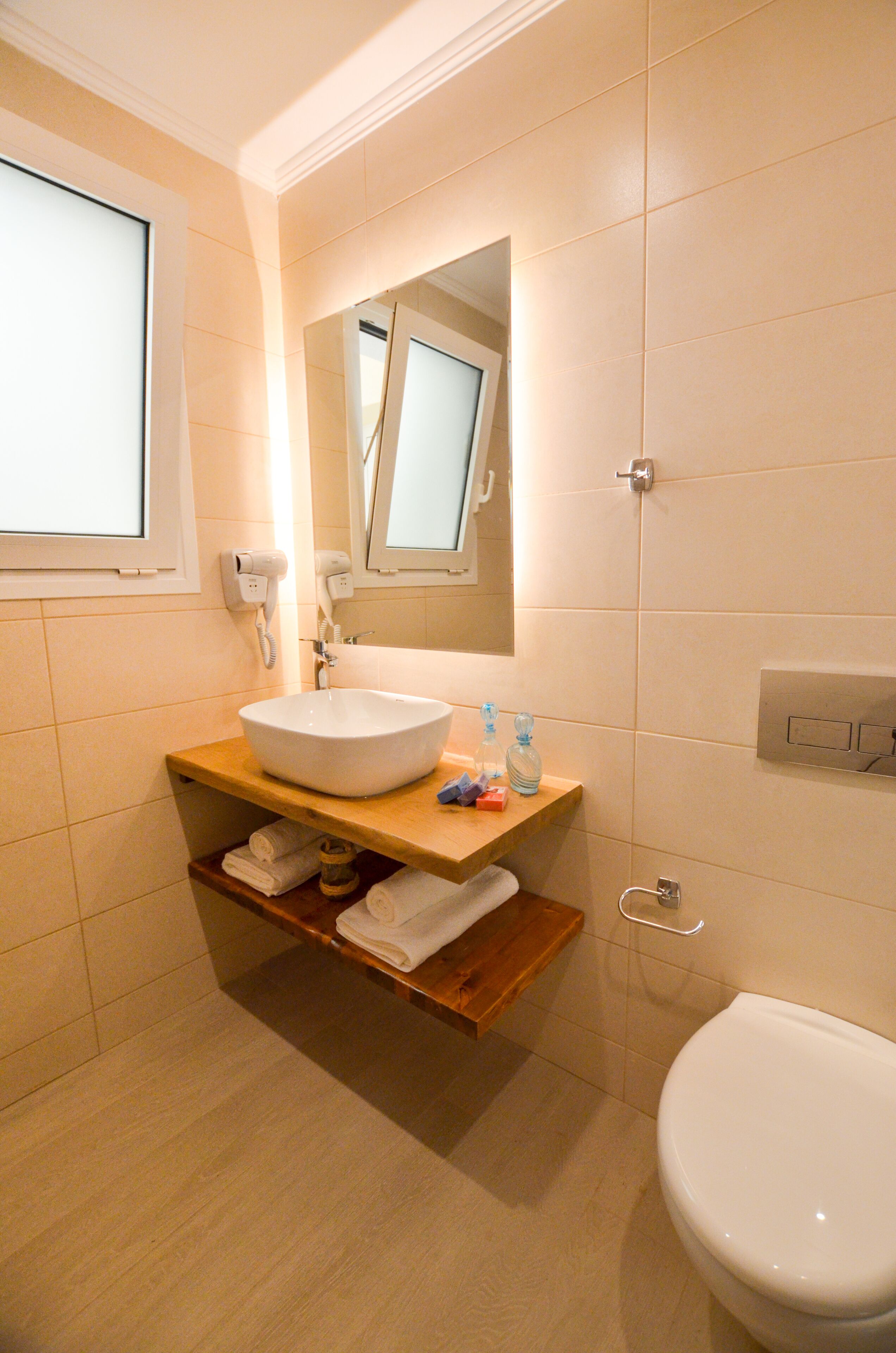 A bathroom with a white sink, a mirror above it, a toilet, and a window.