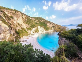 Un paisaje costero con una playa de arena, acantilados rocosos y un mar azul cristalino.