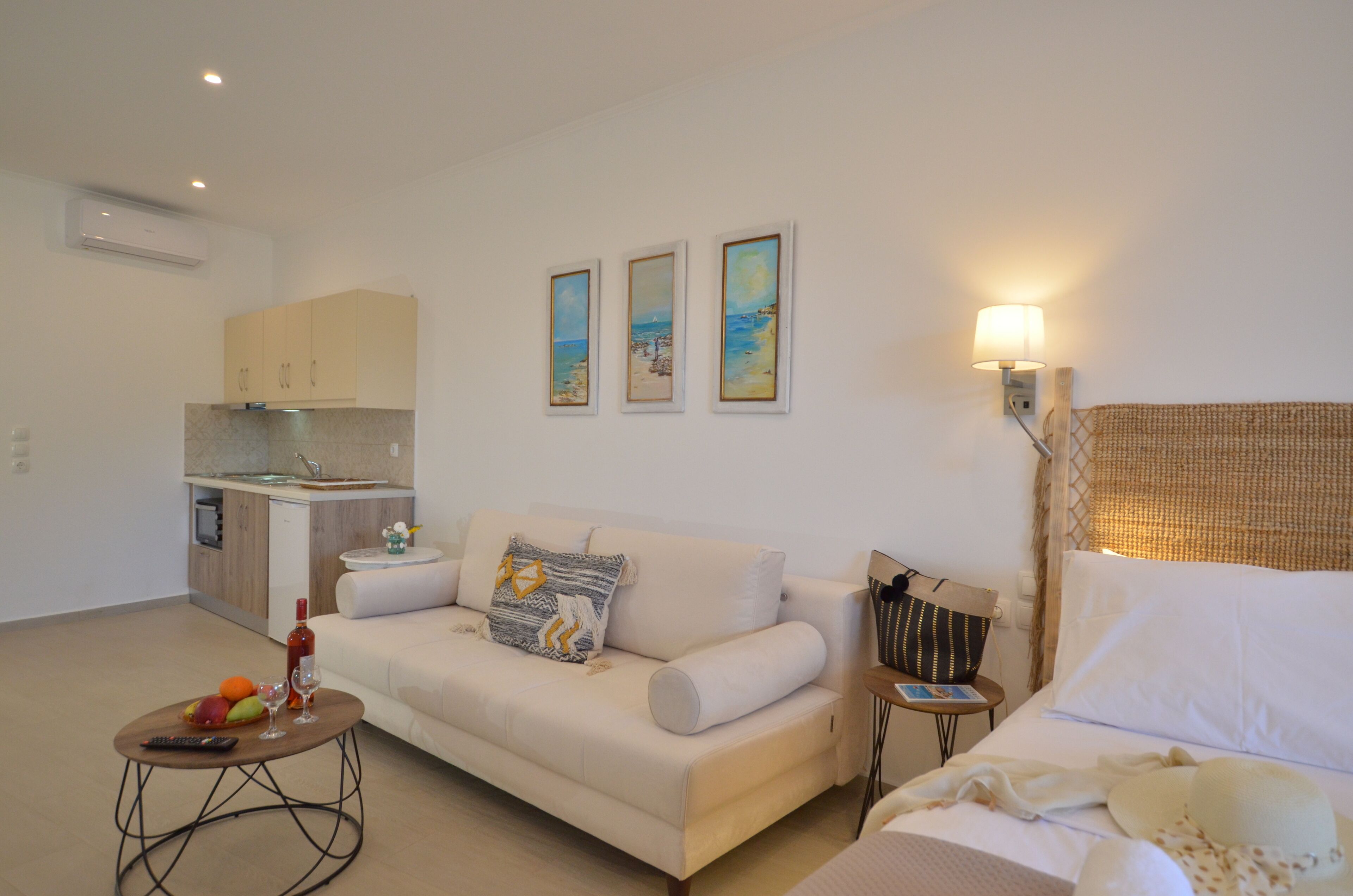 A modern living room with a sofa, a small coffee table, and a bed. There is a kitchen area with cabinets and a sink. Three framed pictures are hung on the wall.
