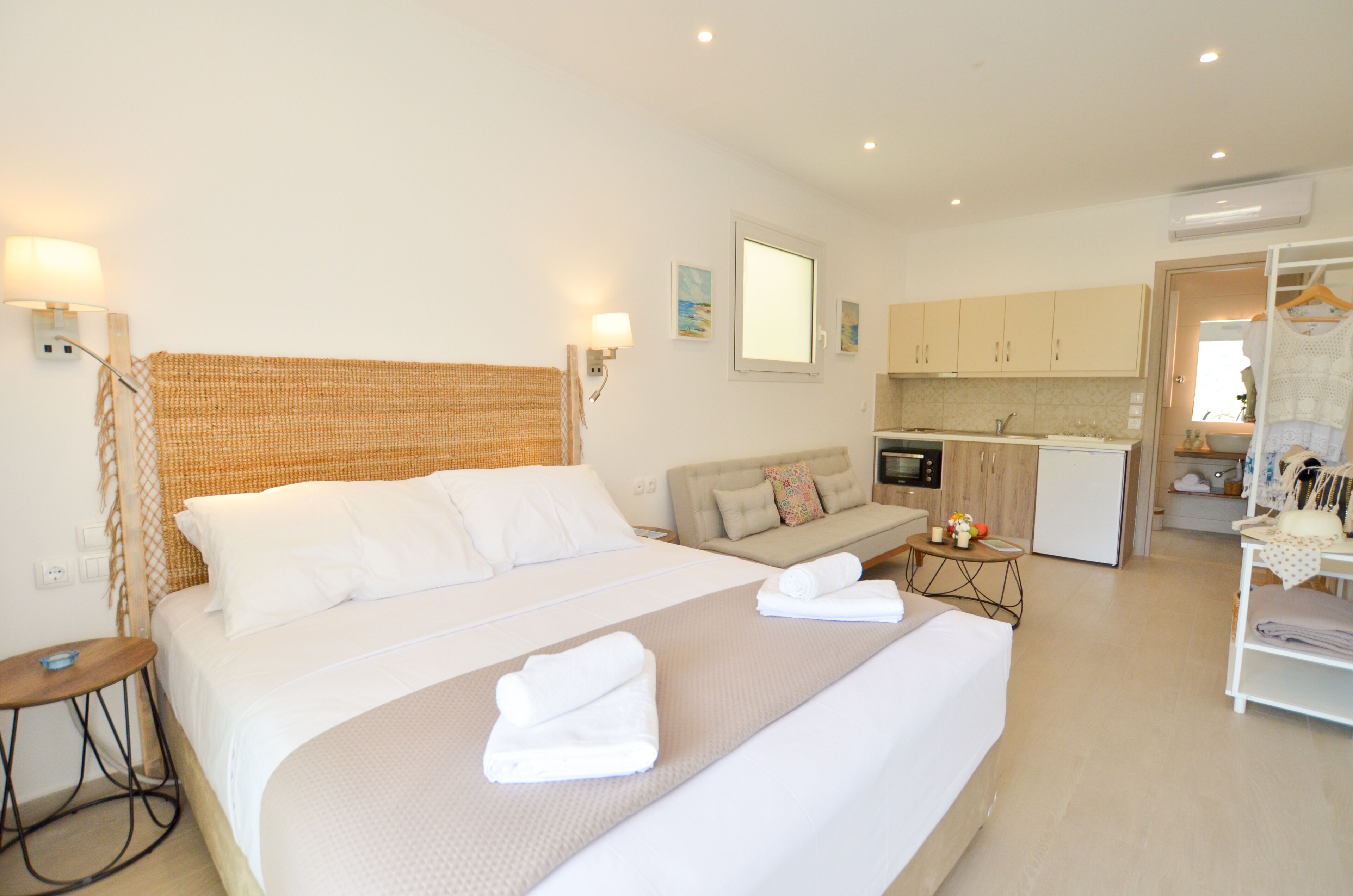 A hotel room with a large bed, a sofa, a small table, and a kitchenette.