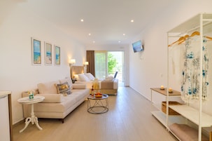 Una sala moderna con un sofá, una mesita de centro y un televisor montado en la pared. Se ve una ventana con cortinas y vistas a la vegetación exterior.