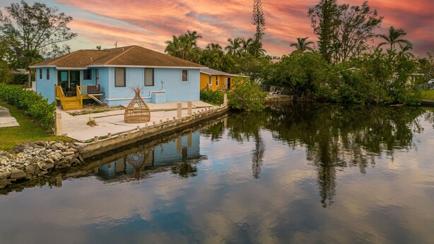 A house by a calm water body with a clear sky. - 🏖️4 BR Canal Front Oasis- 1.5 Miles to Downtown! (Naples)