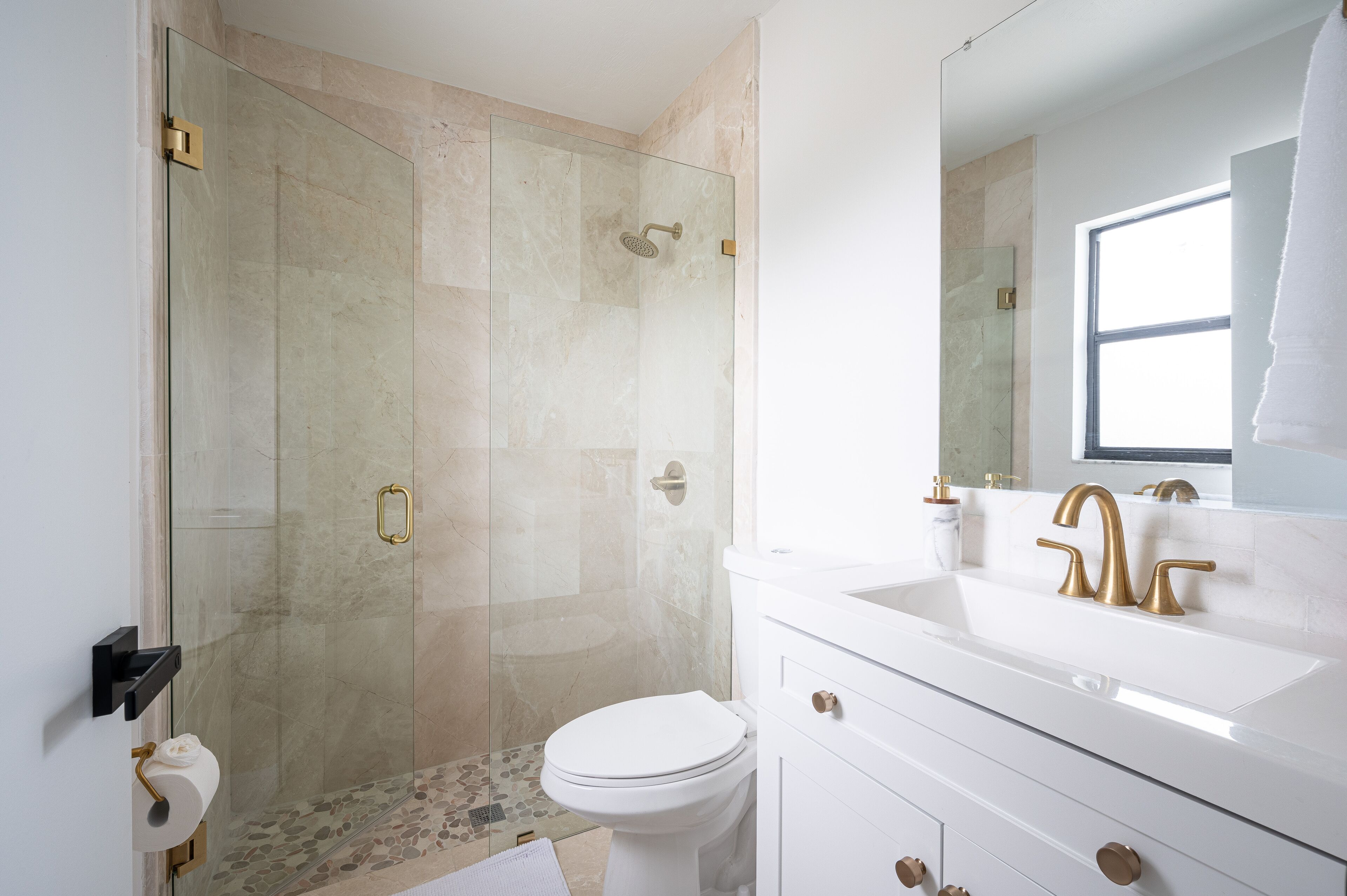 Ein modernes Badezimmer mit einer Glaskabine zur Dusche, einem weißen Waschbecken mit goldfarbenen Armaturen und einer Toilette.