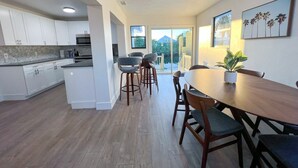 A modern kitchen with white cabinets and a wooden countertop, a dining area with a wooden table and chairs, and a large window with a view of greenery. - 🏖️4 BR Canal Front Oasis- 1.5 Miles to Downtown! (Naples)