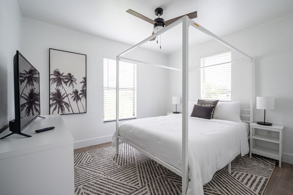A bedroom with a four-poster bed, a TV on a stand, and a ceiling fan.