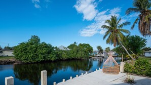 A waterfront view with a concrete dock, a wicker chair, and palm trees. - 🏖️4 BR Canal Front Oasis- 1.5 Miles to Downtown! (Naples)