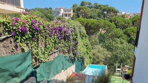 A stone staircase leading to a pool area, surrounded by vibrant flower beds and a view of a hillside with trees and buildings.