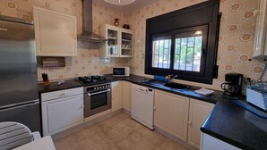 A compact kitchen with white cabinets, a stainless steel refrigerator, a gas stove, a microwave, and a window with a black frame.