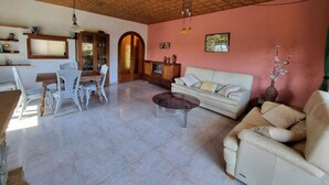 A spacious living room with a wooden ceiling, a dining area with white chairs, a sofa, and a coffee table.
