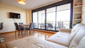 A modern living room with a sofa, dining table, chairs, and a TV mounted on the wall. - 3082 RES LOMAS DE CAMPOAMOR (Orihuela Costa)