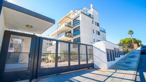 A modern building with a glass entrance, a balcony on the upper floor, and a clear sky. - 3082 RES LOMAS DE CAMPOAMOR (Orihuela Costa)