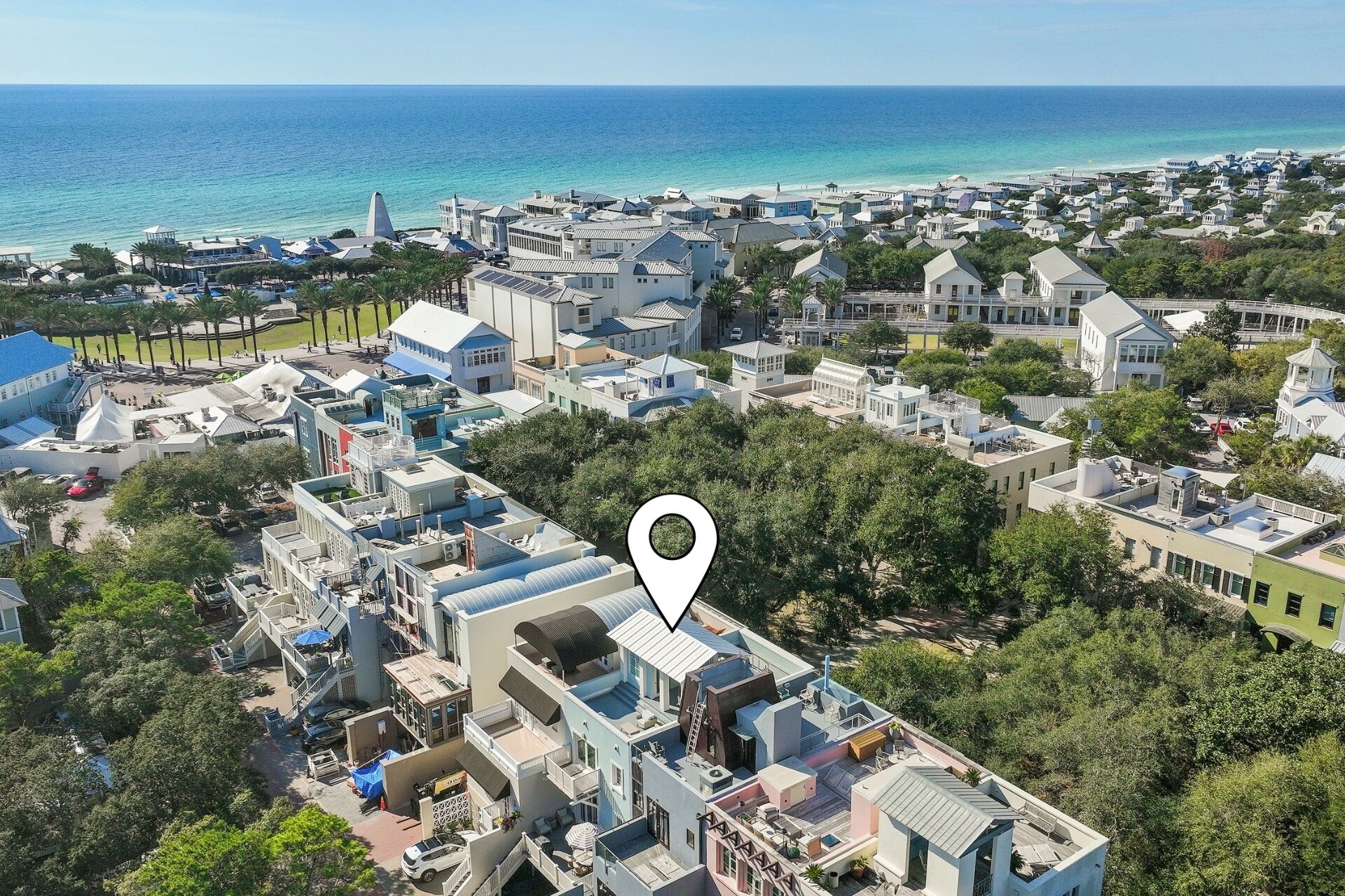 An aerial view of a coastal town with a mix of residential and commercial buildings, a clear view of the ocean, and a location marker indicating a specific area.