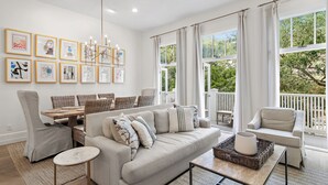 A spacious living room with a large window, a sofa, a dining table, and a chandelier.