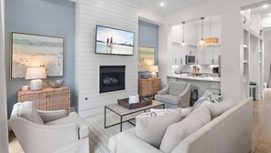 A modern living room with a fireplace, a television, and a kitchen area in the background.