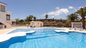 Una piscina con sillas de descanso, un pequeño edificio y un muro de piedra con palmeras.