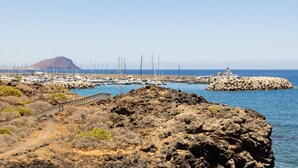 Una zona costera rocosa con un puerto deportivo, barcos y un faro.