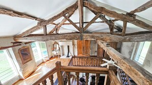 Un intérieur rustique avec des poutres apparentes, un escalier en bois orné de balustres et un bureau blanc avec un miroir.