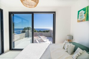 Un dormitorio con una cama grande, vistas al mar y un balcón con sillones de descanso.